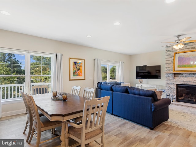 dining room with a fireplace, light wood-type flooring, and ceiling fan