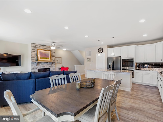 dining space featuring a fireplace, light hardwood / wood-style flooring, and ceiling fan