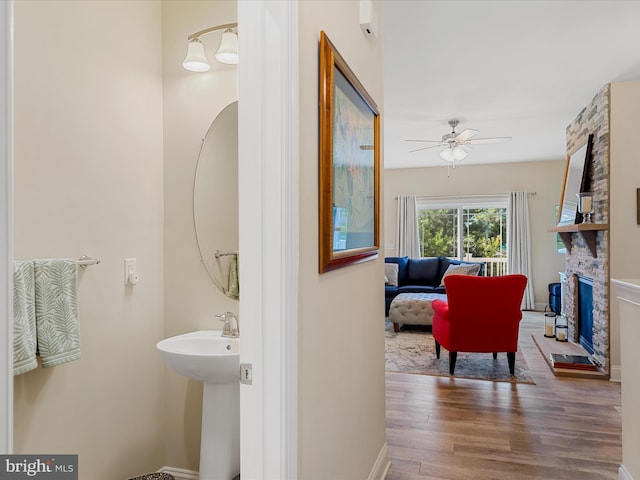 bathroom featuring a stone fireplace, ceiling fan, sink, and wood-type flooring