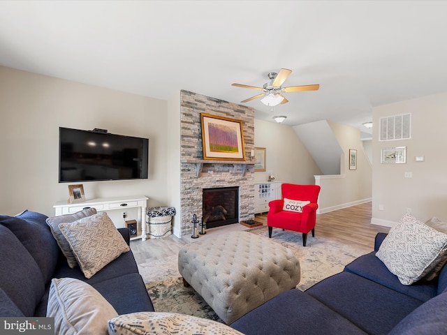 living room with a stone fireplace, ceiling fan, and light hardwood / wood-style flooring