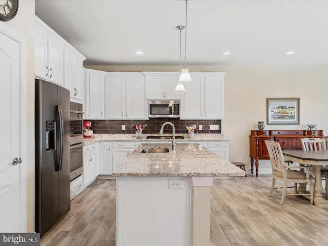 kitchen featuring appliances with stainless steel finishes, light wood-type flooring, sink, pendant lighting, and a center island with sink