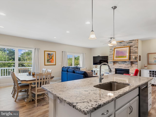 kitchen with white cabinetry, sink, hanging light fixtures, an island with sink, and light hardwood / wood-style floors