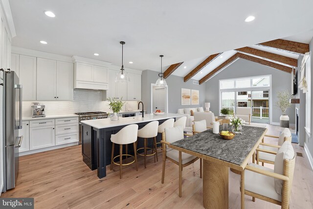 kitchen with stainless steel refrigerator, light hardwood / wood-style flooring, vaulted ceiling with beams, hanging light fixtures, and a center island with sink