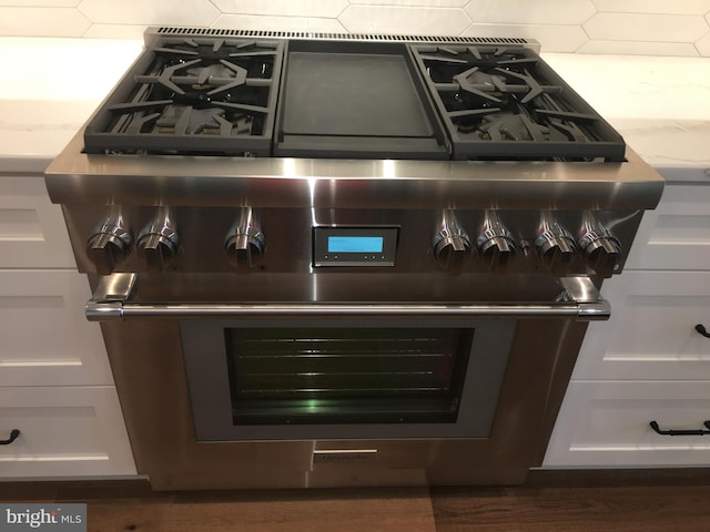 room details featuring high end stainless steel range oven, light stone countertops, decorative backsplash, and white cabinets