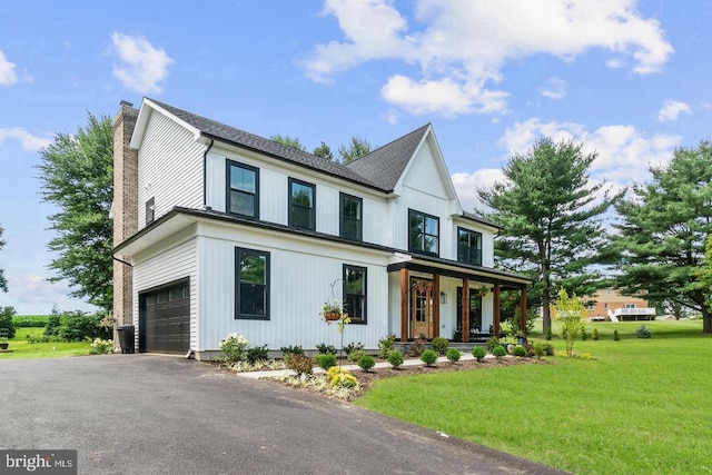 modern inspired farmhouse featuring aphalt driveway, a chimney, an attached garage, a front yard, and covered porch