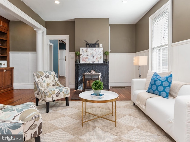 living room featuring a high end fireplace, light hardwood / wood-style floors, and ornate columns