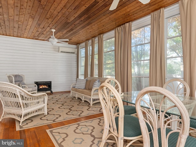 sunroom with a wall mounted AC, ceiling fan, wood ceiling, and a wood stove