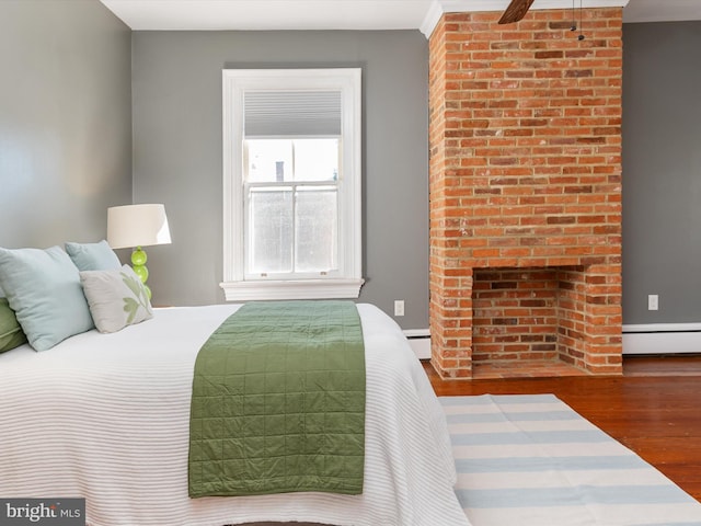 bedroom featuring hardwood / wood-style floors, a baseboard radiator, and a brick fireplace