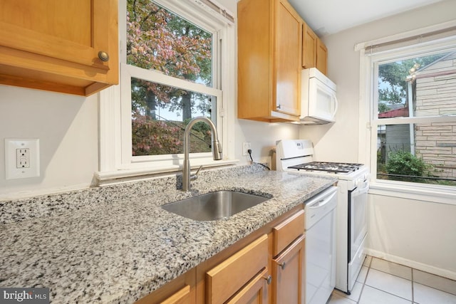 kitchen featuring a wealth of natural light, sink, light stone counters, and white appliances