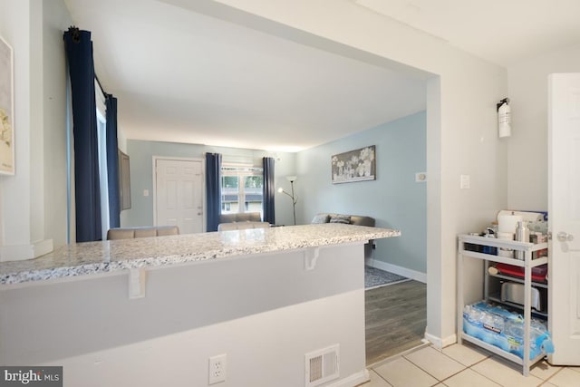 kitchen featuring light hardwood / wood-style floors, kitchen peninsula, light stone countertops, and a breakfast bar