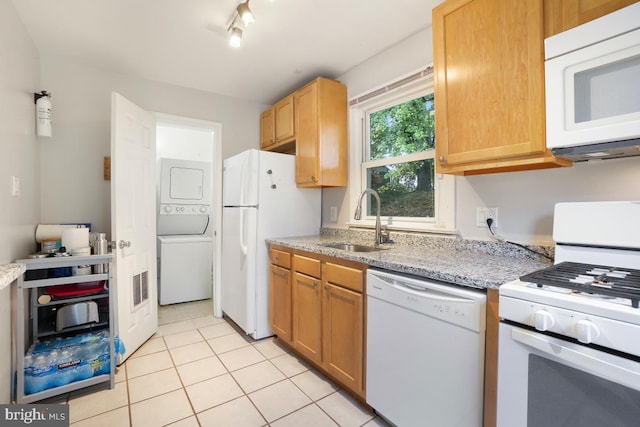 kitchen with rail lighting, light tile patterned floors, stacked washing maching and dryer, sink, and white appliances