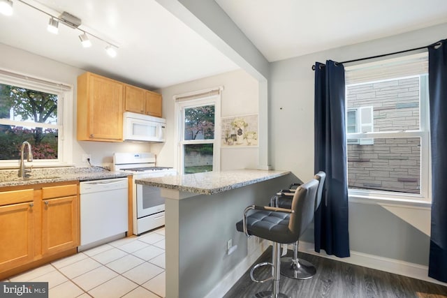 kitchen featuring kitchen peninsula, light stone countertops, a kitchen bar, sink, and white appliances