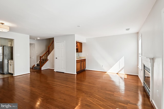 unfurnished living room with stairway, baseboards, visible vents, dark wood finished floors, and a glass covered fireplace