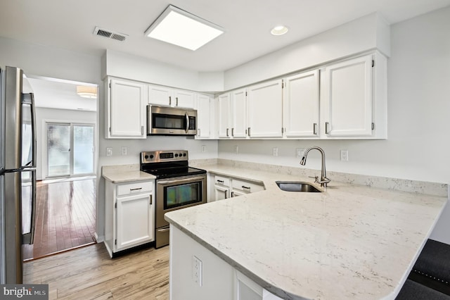 kitchen with visible vents, a sink, appliances with stainless steel finishes, a peninsula, and light stone countertops