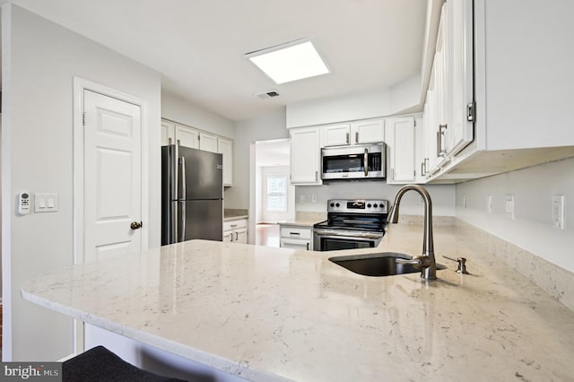 kitchen with light stone counters, visible vents, a peninsula, a sink, and appliances with stainless steel finishes