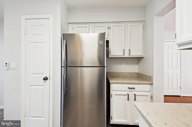 kitchen with white cabinets, light stone countertops, and freestanding refrigerator