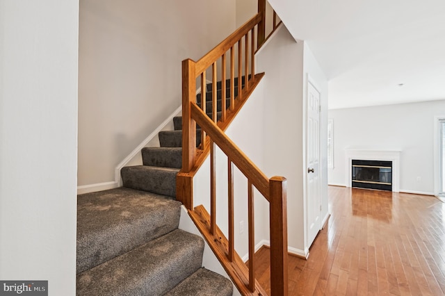 stairs with baseboards, a glass covered fireplace, and hardwood / wood-style flooring