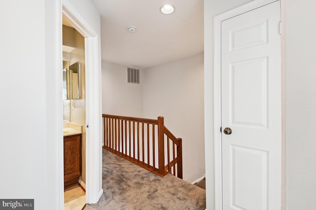 hallway with an upstairs landing, visible vents, and light colored carpet