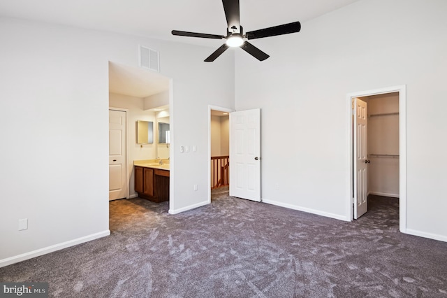 unfurnished bedroom with a spacious closet, baseboards, visible vents, and dark colored carpet