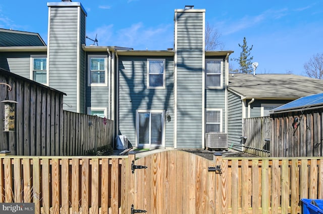 rear view of property featuring a gate, a chimney, and fence