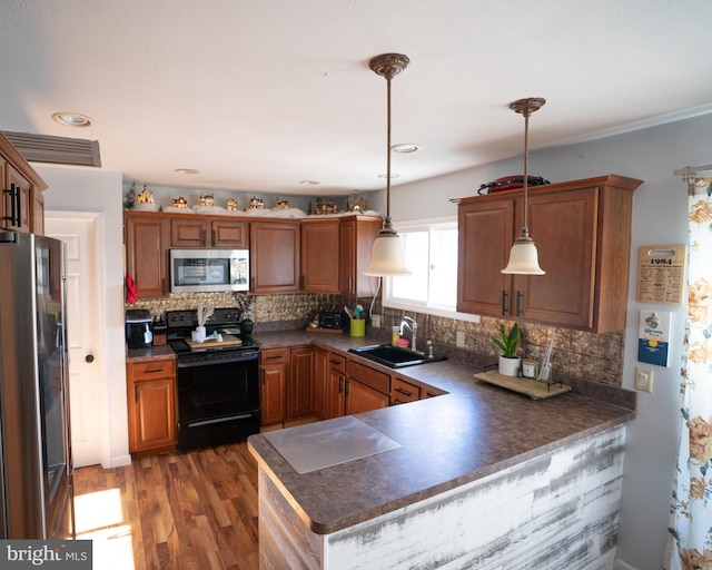 kitchen with decorative backsplash, wood finished floors, a peninsula, stainless steel appliances, and a sink