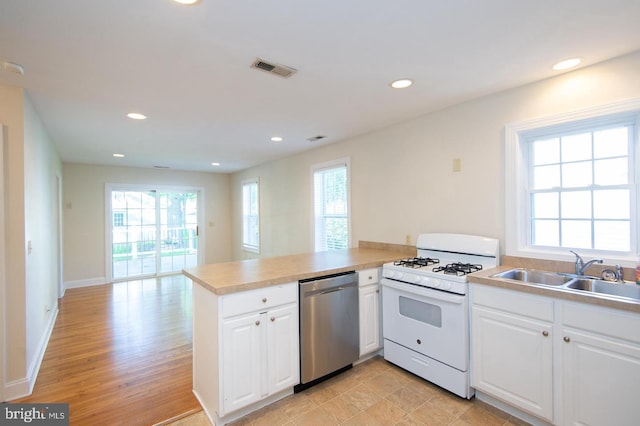 kitchen with a wealth of natural light, white gas range oven, kitchen peninsula, and stainless steel dishwasher