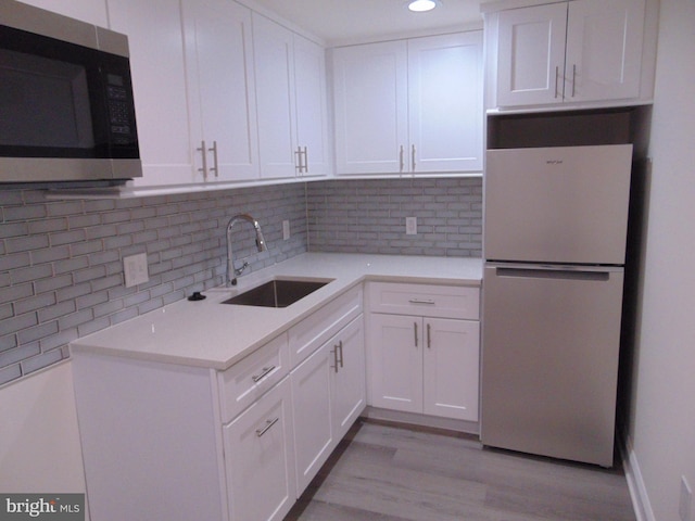 kitchen with sink, tasteful backsplash, white cabinetry, light wood-type flooring, and white fridge