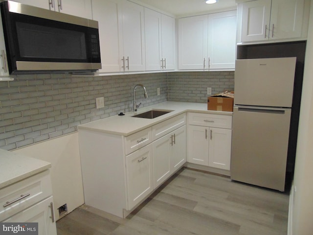 kitchen with sink, backsplash, white cabinetry, light wood-type flooring, and white fridge