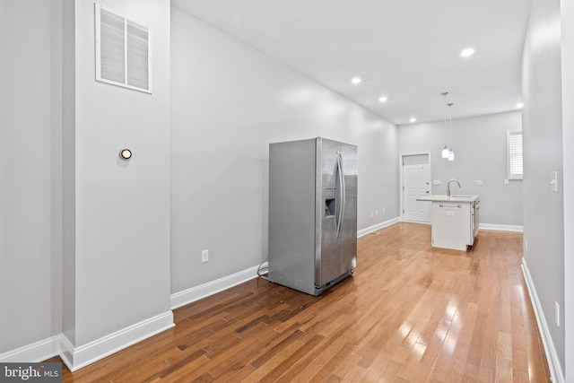 kitchen featuring hanging light fixtures, stainless steel fridge, light hardwood / wood-style floors, and an island with sink