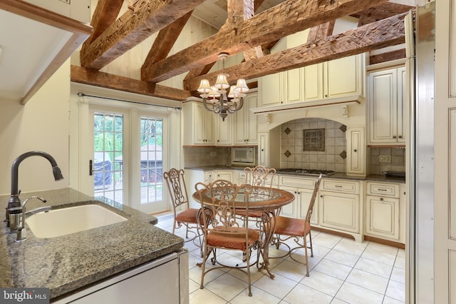 kitchen with dark stone counters, cream cabinets, sink, and a chandelier