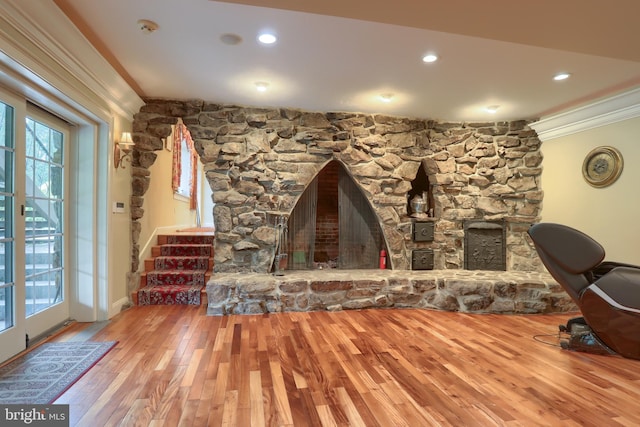 living room with crown molding, hardwood / wood-style flooring, and a stone fireplace