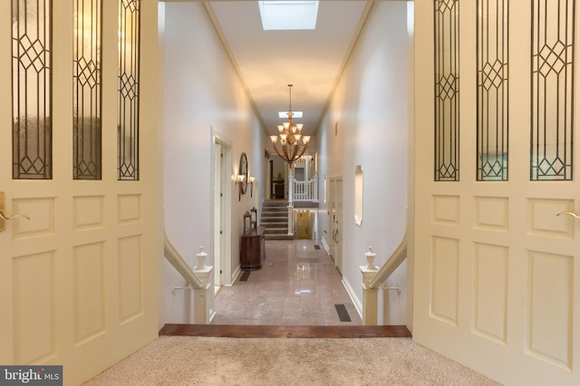 foyer entrance with a notable chandelier, a skylight, carpet floors, and ornamental molding