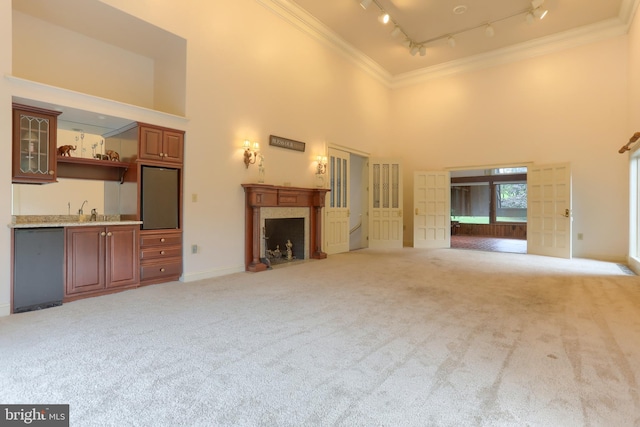 unfurnished living room with light colored carpet, a towering ceiling, track lighting, and crown molding