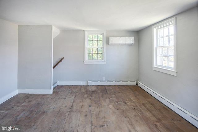 unfurnished room with a baseboard radiator, a wall unit AC, hardwood / wood-style flooring, and a healthy amount of sunlight