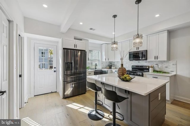 kitchen with beamed ceiling, white cabinetry, stainless steel appliances, a center island, and light hardwood / wood-style floors