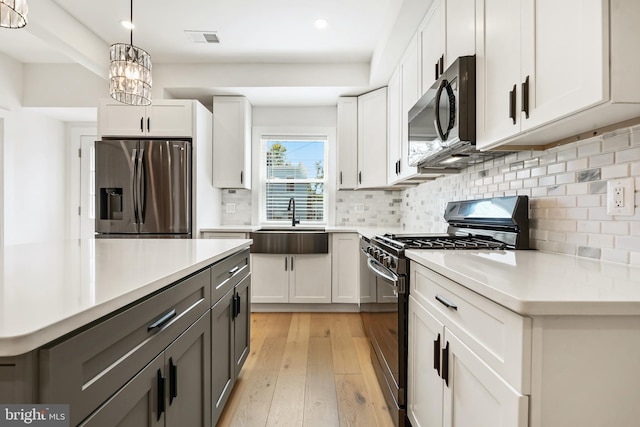 kitchen with pendant lighting, a notable chandelier, appliances with stainless steel finishes, white cabinetry, and light wood-type flooring