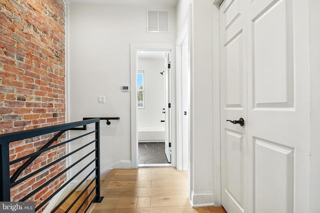 corridor featuring light wood-type flooring and brick wall