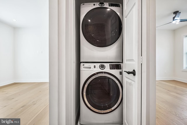 laundry area featuring stacked washer / dryer and light hardwood / wood-style flooring