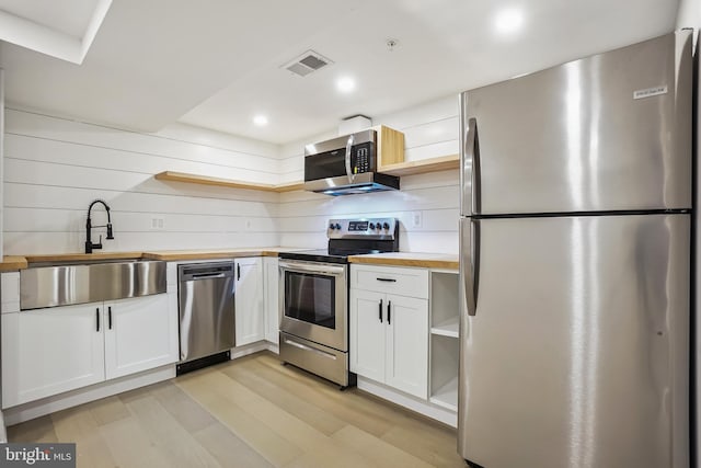 kitchen with butcher block countertops, light hardwood / wood-style flooring, stainless steel appliances, sink, and white cabinets