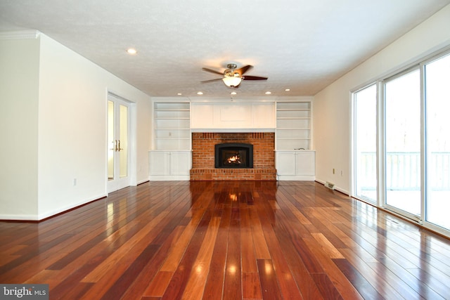 unfurnished living room with ceiling fan, a brick fireplace, built in features, wood-type flooring, and a textured ceiling