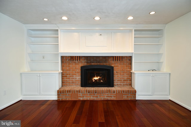 unfurnished living room featuring dark hardwood / wood-style flooring, built in features, and a brick fireplace