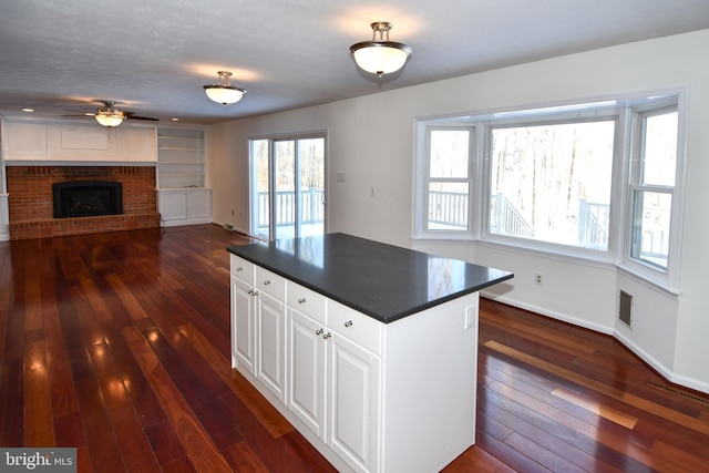 kitchen featuring a brick fireplace, dark hardwood / wood-style floors, white cabinetry, and ceiling fan