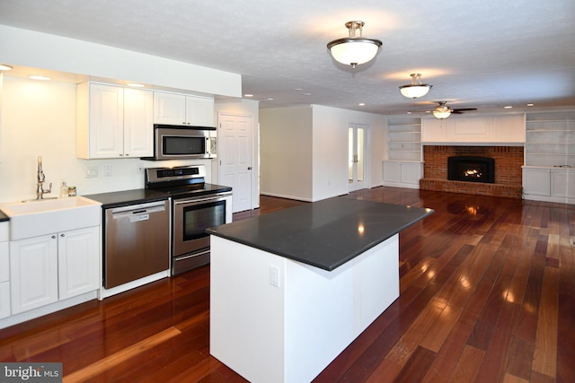 kitchen featuring white cabinets, sink, ceiling fan, a fireplace, and appliances with stainless steel finishes