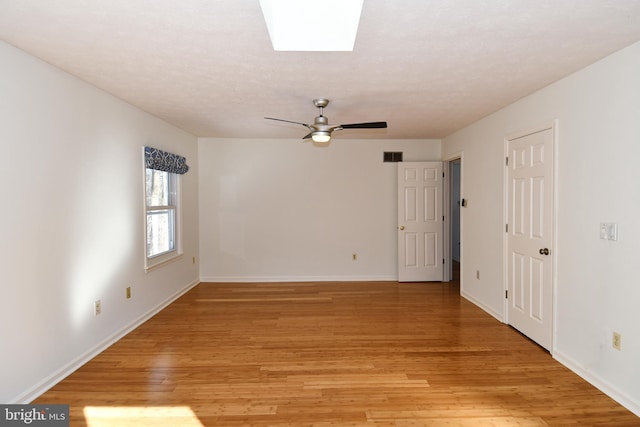 empty room featuring a skylight, ceiling fan, and light wood-type flooring