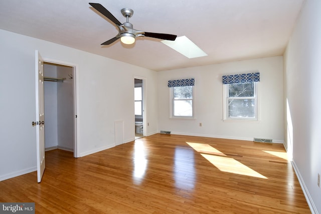 unfurnished bedroom with a skylight, ceiling fan, ensuite bathroom, light hardwood / wood-style floors, and a walk in closet