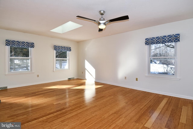 unfurnished room featuring a skylight, ceiling fan, and light wood-type flooring