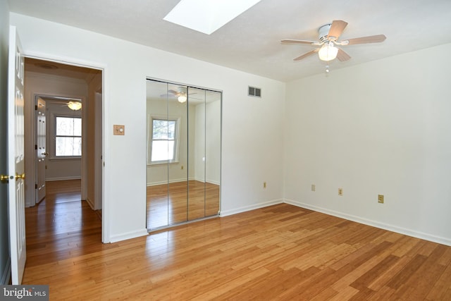 unfurnished bedroom featuring a closet, a skylight, light hardwood / wood-style flooring, and ceiling fan