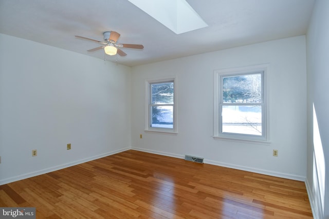 spare room with light wood-type flooring, a skylight, and ceiling fan