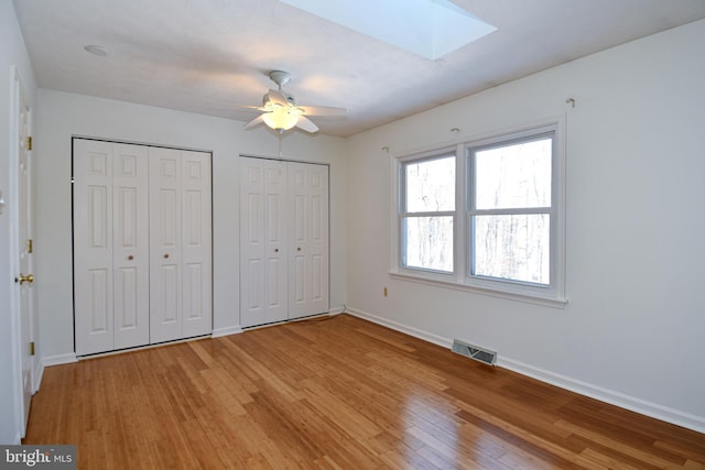 unfurnished bedroom featuring a skylight, light hardwood / wood-style floors, ceiling fan, and multiple closets