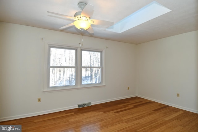 empty room featuring ceiling fan, wood-type flooring, and a skylight